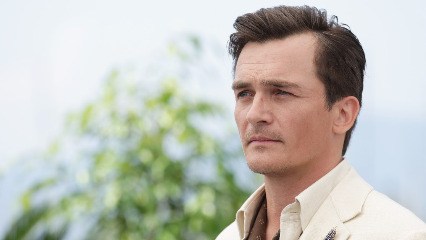Rupert Friend joins the “photo booth” opposite Lily James and Raffey Cassidy